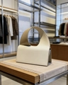 Detail of minimalist cream leather handbag with unique circular integrated handle on wood - White