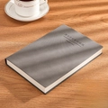 Dark gray A5 business notebook in sheepskin texture leather on a desk with a coffee cup - Ruled / A5-Grey
