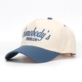 Dettaglio del ricamo Somebody's Problem su un cappellino da baseball bicolore - Beige/Blu Grigio