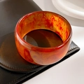 Close-up of retro amber resin bangle with marbled texture on leather and ceramic background - Coffee Amber Pattern