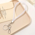 Close-up of white glitter lanyard keychain with silver metal clasp on a minimalist tray - White