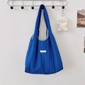 Detail der blauen gesteppten Plissee-Schultertasche mit Logo-Label an weißer Wand - Blau
