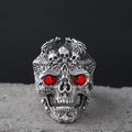 Detailed close-up of gothic skull ring with red gemstone eyes on a textured stone surface - Red Eye Skull