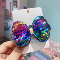 Close-up of a colorful sequined bow hair clip with iridescent finish on a card - Multicolor