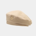 Detailansicht einer klassischen beigen Baskenmütze mit goldenem Metallabzeichen 'C' - Khaki