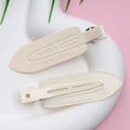 Close-up of two cream matte duckbill hair clips with embossed lettering on white plate - Creamy White - Glossy with Letters