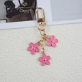 Golden keychain featuring three pink flower pendants on a textured white background - Rose Red