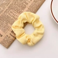 Bloemige kant scrunchie met wafeltextuur lichtgeel op een vintage krant achtergrond - Gembergeel