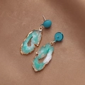 Close-up of green irregular resin earrings with gold edges on brown fabric background - Green