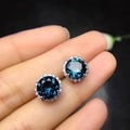 Sparkling sapphire blue stud earrings with silver pins shown on fingertip - Blue Diamond Flower Earrings Tz-24