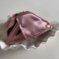 Detail einer rosa Satin-Haarklammer mit Goldetikett auf weißem Muschelteller - Rosa