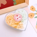 Close-up of heart-shaped storage box filled with yellow and green elastic hair bands - Yellow + Green