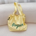 Dettaglio di borsa tote gialla con coulisse e scritta Bonjour verde su tessuto tela - Giallo