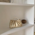Détail d'un sac à main doré plissé avec poignée en perles sur un support blanc - Doré