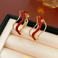 Vista macro de pendientes ondulados dorados con esmalte rojo sobre cojín de joya - Bañado en Oro Oro Rojo (Aguja de Plata)