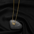 Golden Leo zodiac necklace with vintage letter pendant on black silk and pebble background - Leo Gold