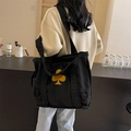 Large black canvas tote bag with yellow clover patch and frayed edges worn by a model - Raw Edge Clover Patch Style / Black