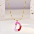 Detail van een gouden ketting met roze en lila emaille D-hanger op een stenen achtergrond - Letter D