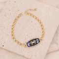 Macro detail of gold Cancer zodiac bracelet featuring blue enamel and purple zircon inlay - Cancer