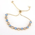 Detail eines goldenen Armbands mit blauem Evil-Eye-Herz und lila Zirkon-Elementen - Blau