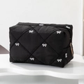 Detail of black quilted makeup bag featuring white bow embroidery and gold zipper - Black
