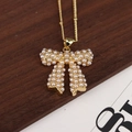 Elegante collar de oro con colgante de lazo y perlas blancas sobre fondo de madera - Collar