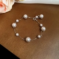 Detailansicht eines unregelmäßigen Perlenarmbands mit Silberkette auf Holzoberfläche - Silbernes Einfaches Weißes Perlenarmband / Silber/Weiß