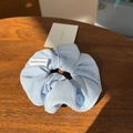 Close-up of light blue fabric scrunchie with button detail on dark wooden desk - Blue Button Scrunchie