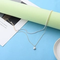 Detail view of double-layer gold chain and pearl bracelet on a light green stand - Necklace 13 / Gold