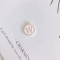Macro view of a round pink enamel pendant with gold letter W for DIY jewelry making - Letter W