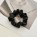 Vue détaillée d'un chouchou en satin noir avec des plis en tissu doux sur fond neutre - Nouveau Noir