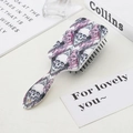 Close-up of skull and pink rose pattern on the back of a cushioned massage hairbrush - Three Skulls