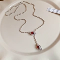 Detailed macro view of silver Y-shaped necklace with red zircon teardrop pendants on a plate - Red Zircon Snake Head Style