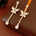 Macro detail of gold butterfly drop earrings with clear zircon on a leather surface - Gold