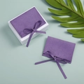 Purple velvet jewelry pouch with bow tie and white gift box on green leaf background - Purple