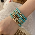 Detail of teal and gold layered beaded bracelets on wrist with boho clay disc charms - Green