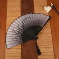 Classic Chinese folding fan with black bamboo frame, orchid ink painting, and silk tassel - Orchid Grass