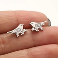 Macro view of bird-shaped stainless steel stud earrings held to show compact size - Steel