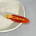 Detail of red and orange matte hair clips placed on a white ceramic plate edge - Orange
