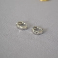 Gros plan détaillé de créoles en argent au motif de bambou sur un fond de tissu gris texturé - Boucle d'oreille Bambou Argentée / Argenté