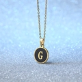 Golden necklace with circular black enamel pendant featuring a stylish gold letter G - Letter G