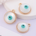 Macro shot of three golden circular evil eye pendants with white resin and teal accents - Round