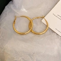 Detailed view of polished large gold hoop earrings on a minimalist white paper background - Medium / Gold