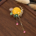 Detail of a Chinese style gourd brooch with yellow resin, enamel flowers and golden tassels - Lotus Tassel