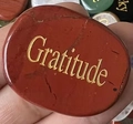 Macro di una pietra naturale rossa con incisione dorata Gratitude nella mano - Diaspro Rosso