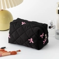Quilted black cosmetic bag with pink bow embroidery and zipper closure on a white desk - Black