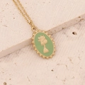 Macro shot of gold portrait pendant with light green enamel inlay on beige stone background - Green