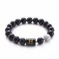 Macro shot of 10mm black onyx bead bracelet with white turquoise and gold letter H charm - Letter H