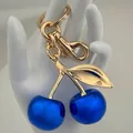 Detailed view of cherry keychain with bright blue beads and gold alloy leaf on hand model - Agate Blue Cherry with Light Gold