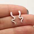 Close-up of minimalist silver snake stud earrings held between fingers for size reference - 674 Snake / Steel